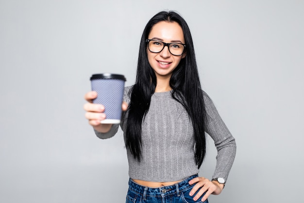 Portret van een mooie meeneemkoffiekop die van de vrouwenholding over grijze muur wordt geïsoleerd