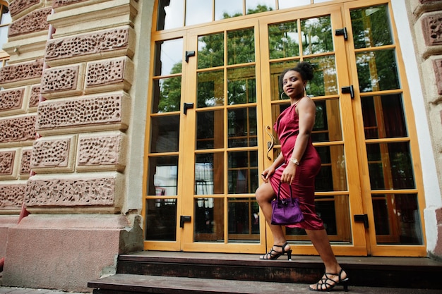 Portret van een mooie natuurlijke jonge Afrikaanse vrouw met afrohaar Zwart model in rode zijden jurk