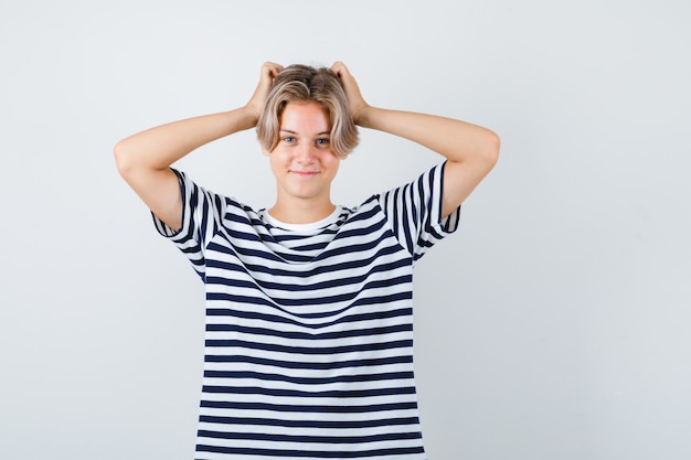 Portret van een mooie tienerjongen met de handen op het hoofd in een gestreept t-shirt en een vrolijk vooraanzicht