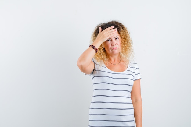 Portret van een mooie vrouw die de hand op het voorhoofd in een t-shirt houdt en er vermoeid uitziet