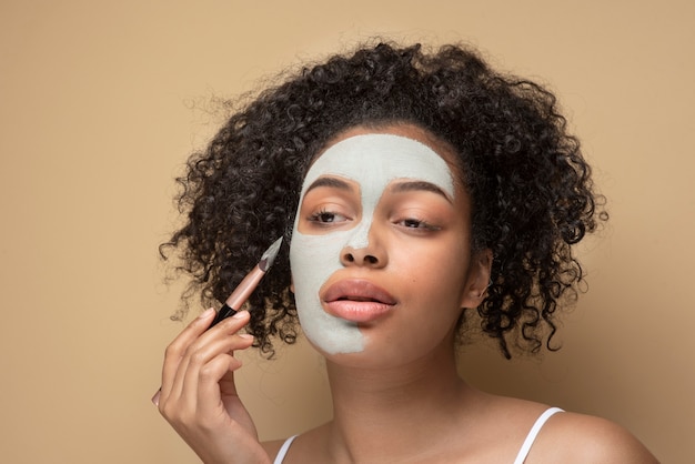 Gratis foto portret van een mooie vrouw die een gezichtsmasker aanbrengt met een make-upborstel op haar gezicht