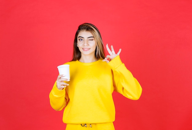 Portret van een mooie vrouw die een plastic kopje thee vasthoudt en een goed teken geeft