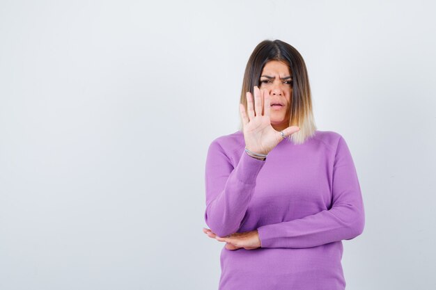 Portret van een mooie vrouw die een stopgebaar in een paarse trui toont en er serieus vooraanzicht uitziet