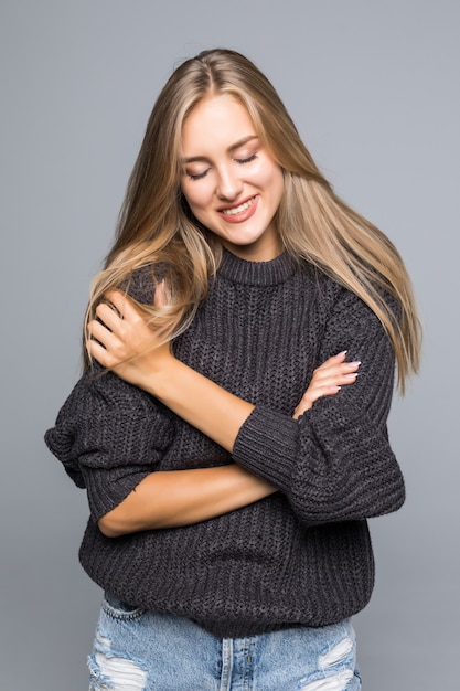Portret van een mooie vrouw die een warme gebreide trui op haar lichaam draagt op een grijze geïsoleerde achtergrond