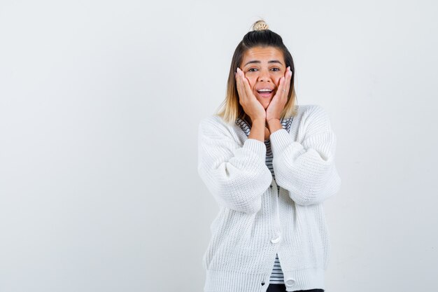 Portret van een mooie vrouw die handen op de wangen houdt in een t-shirt, vest en er vrolijk uitziet