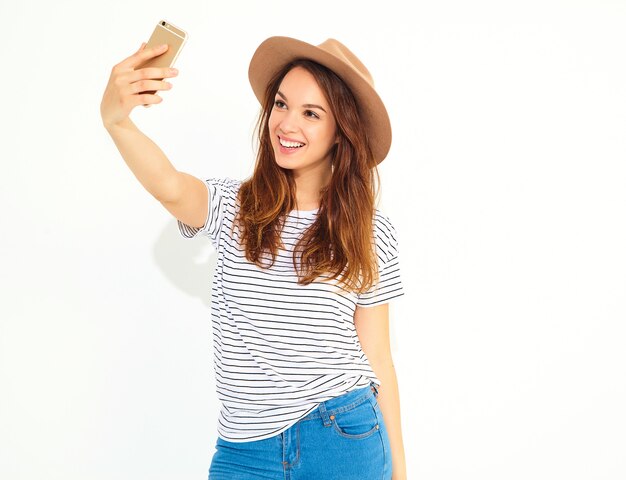Portret van een mooie vrouw in de zomer hipster kleren die een selfie nemen op witte muur wordt geïsoleerd
