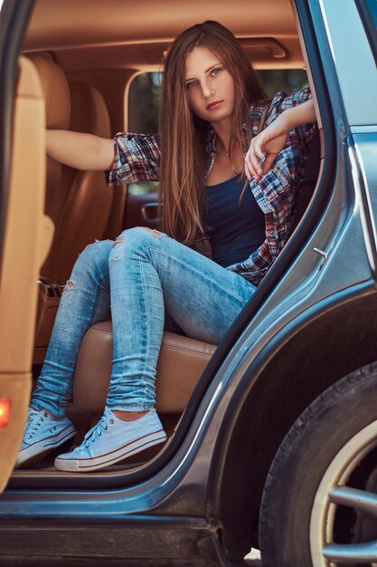 Portret van een mooie vrouw in een fleece shirt en spijkerbroek, zittend in de auto op de achterbank met een open deur.