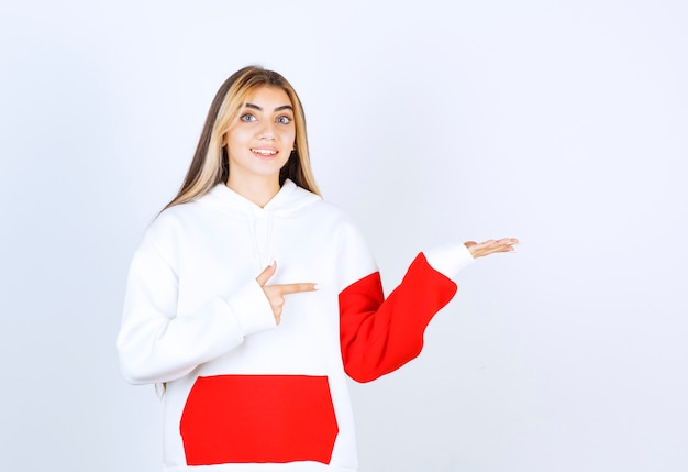 Portret van een mooie vrouw in een warme hoodie die staat en wijst naar de geopende handpalm
