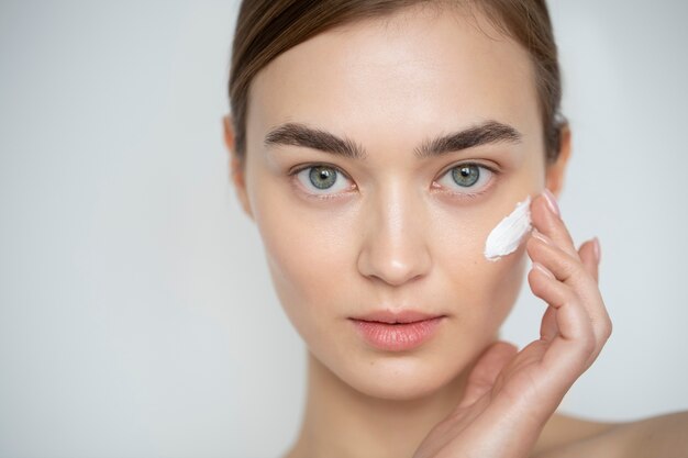 Portret van een mooie vrouw met een heldere huid die een vochtinbrengende crème op haar gezicht gebruikt