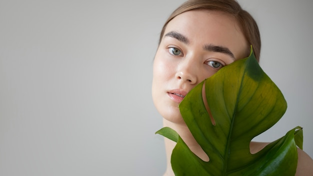 Portret van een mooie vrouw met een heldere huid die poseert met een blad van een monsterplant