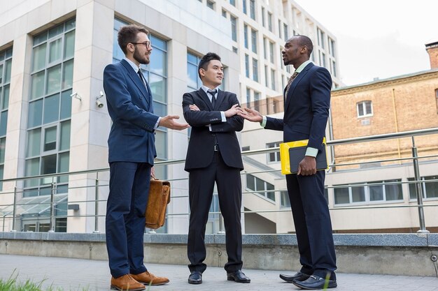 Portret van een multi-etnisch commercieel team. Drie glimlachende mannen die zich tegen de achtergrond van de stad bevinden. De ene man is Europeaan, de andere Chinees en Afrikaans-Amerikaans.