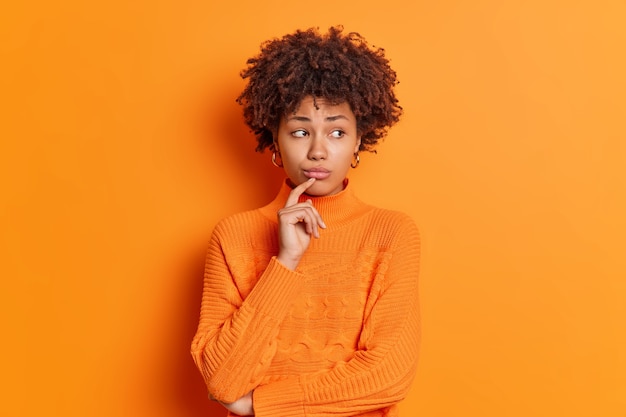 Gratis foto portret van een ongelukkige, bedachtzame, melancholische jonge vrouw voelt zich boos kijkt opzij met een ontevreden uitdrukking denkt na over het oplossen van een probleem geïsoleerd over een oranje muur