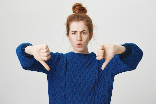 Portret van een ontevreden, niet onder de indruk aantrekkelijk roodharig meisje in een casual wintertrui met duimen naar beneden