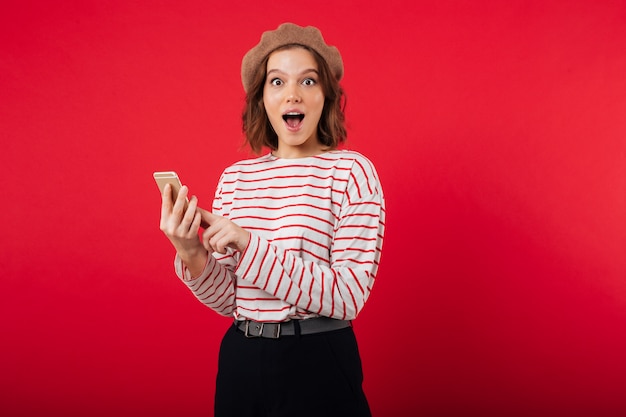 Portret van een opgewekte vrouw die baret draagt die mobiele telefoon houdt