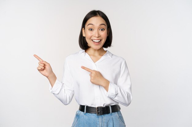 Portret van een opgewonden jonge aziatische vrouw die met de vingers naar de korting wijst en een verkoopbanner toont die op een witte achtergrond staat