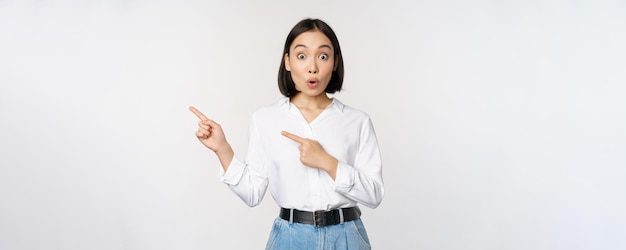 Portret van een opgewonden jonge aziatische vrouw die met de vingers naar de korting wijst en een verkoopbanner toont die op een witte achtergrond staat