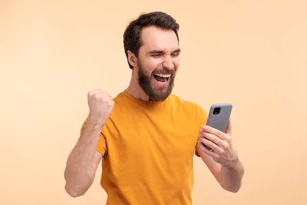 Portret van een opgewonden jongeman die naar zijn smartphone kijkt