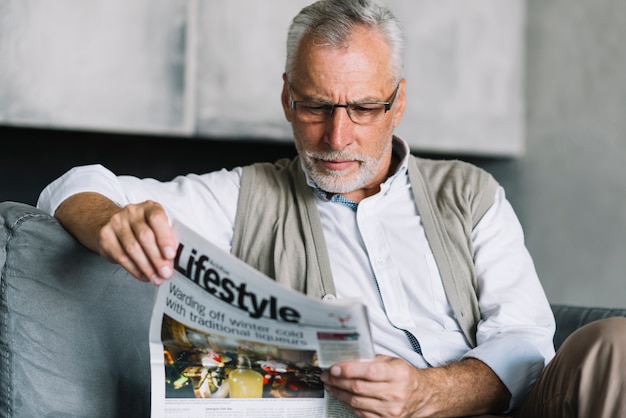 Portret van een oudere man zit op de bank krant lezen