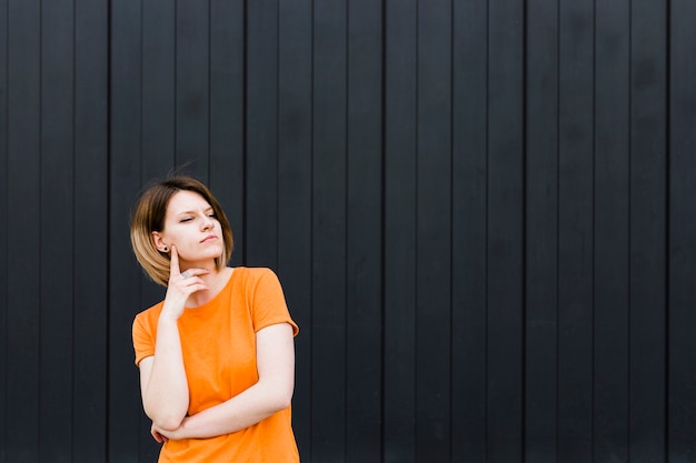 Portret van een overwogen jonge vrouw die zich tegen zwarte muur bevindt