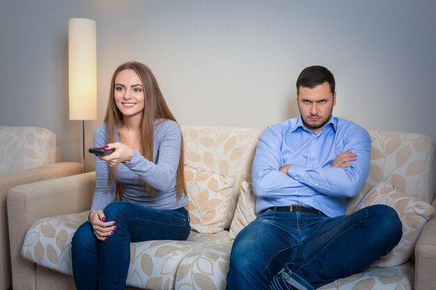 Portret van een paar zittend op de bank televisie kijken. Afbeelding van een gelukkige vrouw met afstandsbediening in handen en een overstuur man