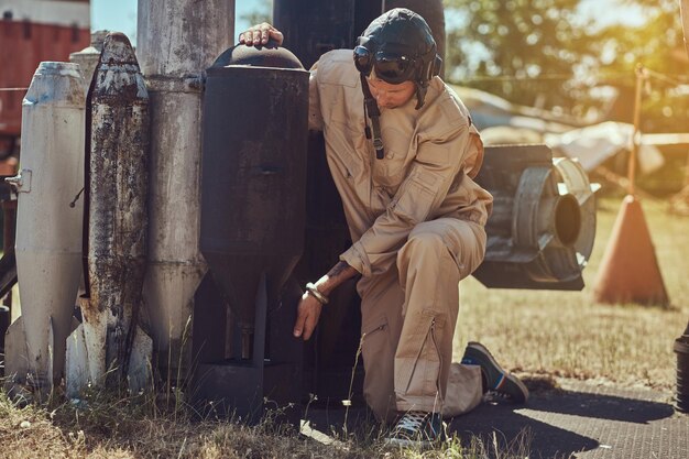 Portret van een piloot in uniform en vliegende helm in de buurt van bommen voor een bommenwerpervliegtuig in een openluchtmuseum.