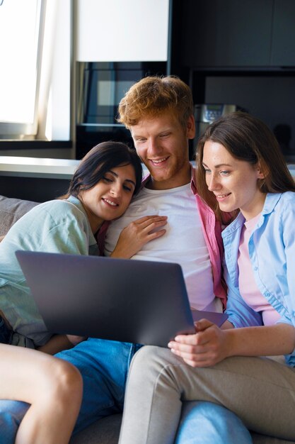 Portret van een polyamorous stel dat thuis op de bank zit en een laptop gebruikt
