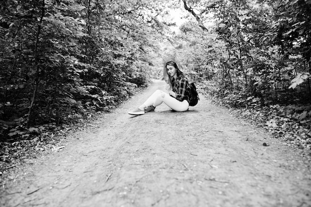 Portret van een positieve jonge, prachtige blonde zittend op de grond met een kaart in haar handen in het bos