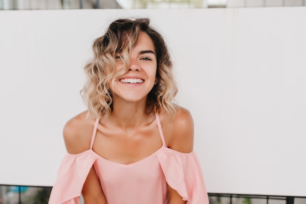 Portret van een prachtig meisje met golvend haar draagt roze kleding. indoor foto van vrolijke kortharige europese vrouw lachen.