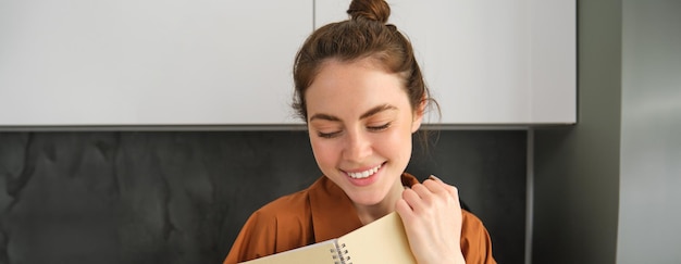 Gratis foto portret van een prachtige jonge vrouw die een student leest die in de keuken staat met een planner die huiswerk doet