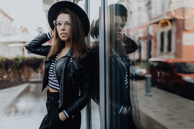 Portret van een prachtige vrouw in de stad na regen in de buurt van schitterende etalages bij koud weer overdag