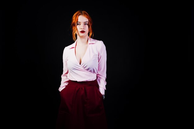 Portret van een roodharig meisje in roze blouse en marsala-rok op de zwarte achtergrond