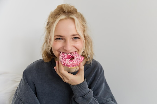 Gratis foto portret van een schattig blond meisje met een roze donut met sprinkles bovenop die haar favoriete eten toont