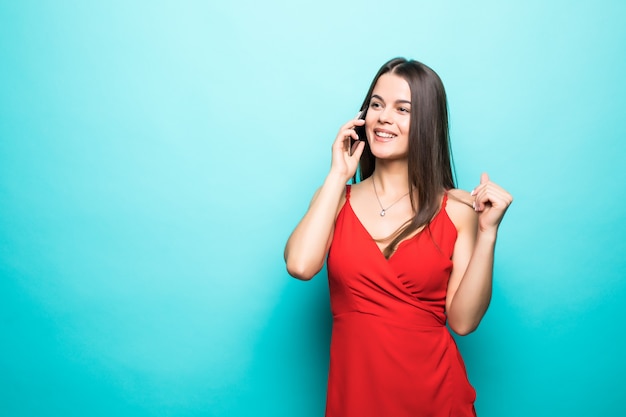 Portret van een schattig gelukkig meisje in jurk praten op mobiele telefoon en lachen geïsoleerd over blauwe muur