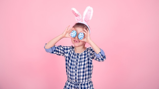 Portret van een schattig klein meisje met paaseieren op een roze achtergrond.