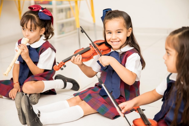 Portret van een schattig Latijns meisje dat viool leert spelen en plezier heeft op de kleuterschool