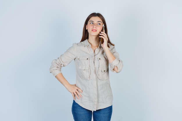 Portret van een schattig meisje dat op een mobiele telefoon praat, wegkijkt in shirt en peinzend kijkt