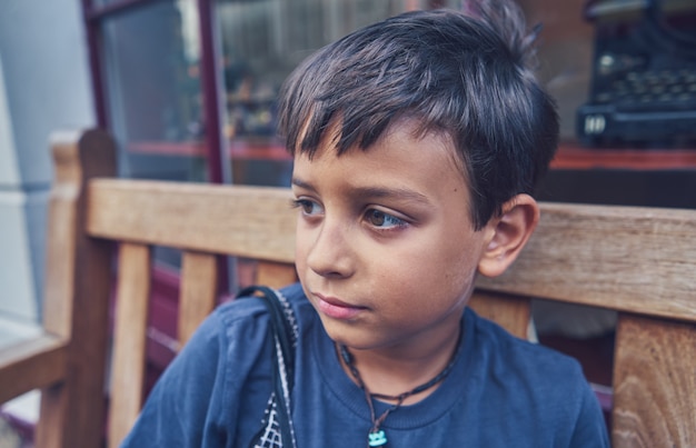 Portret van een schattige kleine jongen die op een bankje zit en denkt