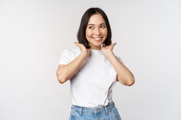 Portret van een schattige, mooie aziatische vrouw die haar nieuwe korte kapsel aanraakt en een kapsel laat zien dat gelukkig glimlacht naar de camera die op een witte achtergrond staat