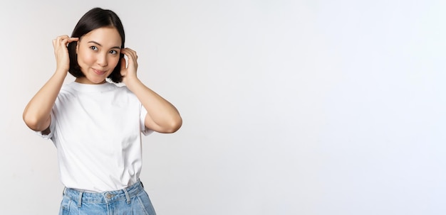 Portret van een schattige, mooie aziatische vrouw die haar nieuwe korte kapsel aanraakt en een kapsel laat zien dat gelukkig glimlacht naar de camera die op een witte achtergrond staat