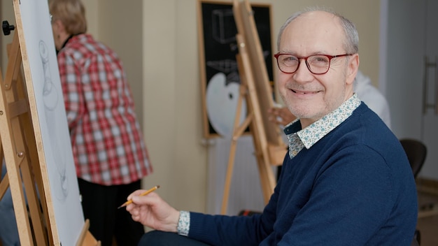 Portret van een senior man die geniet van kunstles om tekenvaardigheden te ontwikkelen voor persoonlijke groei. oudere student die artistieke les bijwoont om meesterwerk op canvas te leren tekenen als goede voornemens voor het nieuwe jaar.