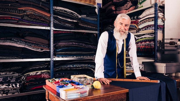 Portret van een senior mannelijke modeontwerper in zijn winkel camera kijken