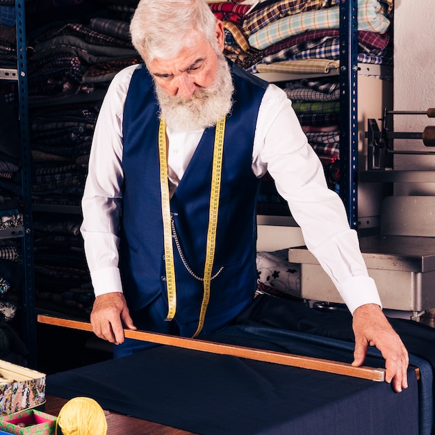 Portret van een senior mannelijke modeontwerper meten stof met houten liniaal