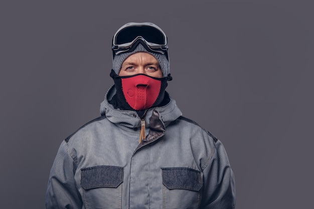 Gratis foto portret van een snowboarder gekleed in een volledige beschermende uitrusting voor extreme snowboarden poseren in een studio. geïsoleerd op de grijze achtergrond.