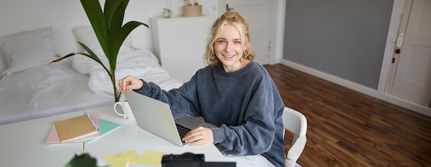Gratis foto portret van een stijlvolle schattige jonge blonde vrouw die met een laptop in een kamer zit en video opneemt op digitaal