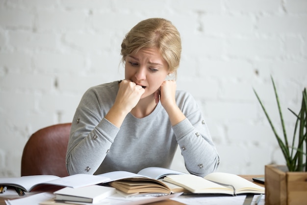 Gratis foto portret van een student meisje zit aan het bureau bijt haar vuist