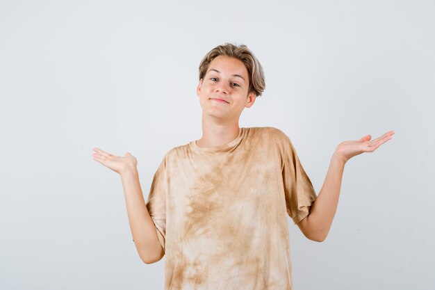 Portret van een tienerjongen die zijn schouders ophaalt in een t-shirt en aarzelend vooraanzicht kijkt