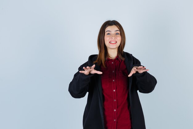 Portret van een tienermeisje dat een weigeringsgebaar in overhemd, jas toont en beschaamd vooraanzicht kijkt