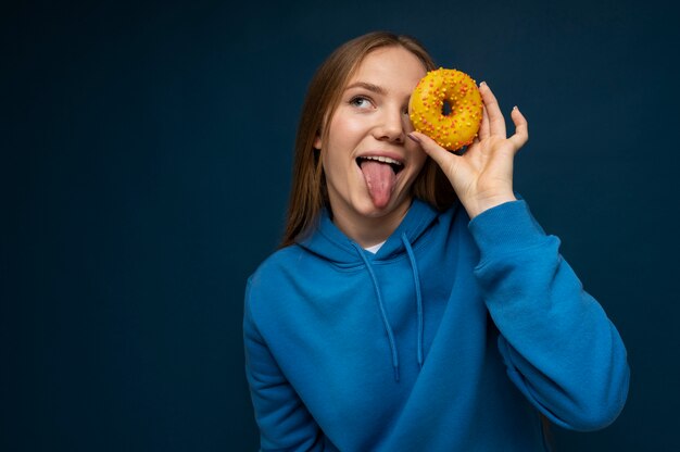 Portret van een tienermeisje dat haar tong uitsteekt en door een donut kijkt