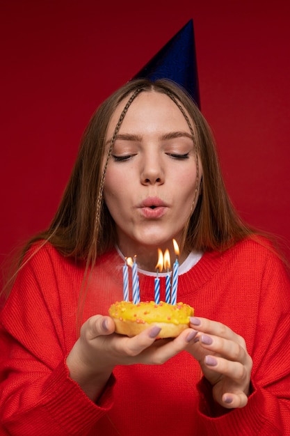 Portret van een tienermeisje dat haar verjaardagskaarsen blaast terwijl ze een verjaardagshoed draagt