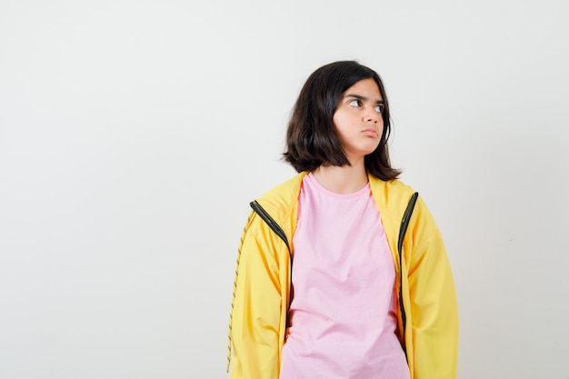 Portret van een tienermeisje dat opzij kijkt in t-shirt, jas en geïnteresseerd vooraanzicht kijkt